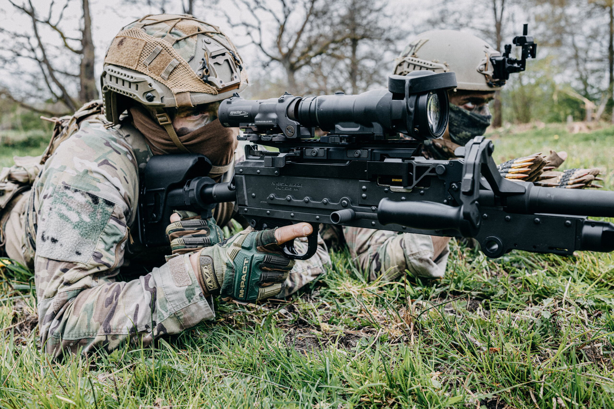 Operators in camouflage gear in prone firing position using an FN MAG® TACTICAL with Long Rail fitted with an optic in an outdoor environment